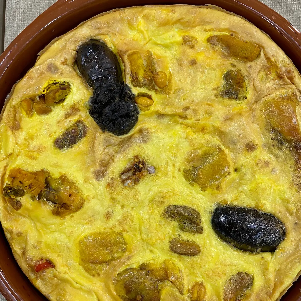 Arroz con costra recién salido del horno en cazuela de barro, visto desde arriba, con la costra de huevo dorada y morcillas asomando